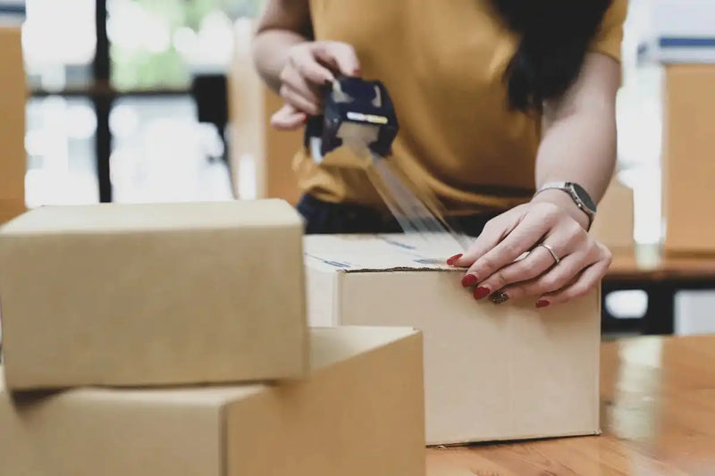Person using a barcode scanner on a cardboard box with other boxes in the foreground.